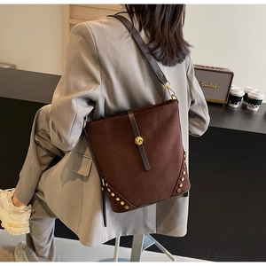 Dettaglio di una borsa a secchiello in pelle scamosciata marrone con borchie dorate e tracolla
