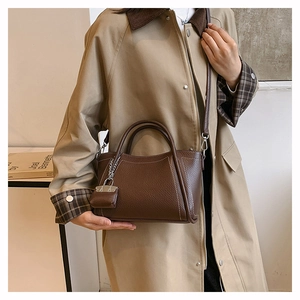 Detail of dark brown lychee leather handbag featuring white stitching and mini charm pendant