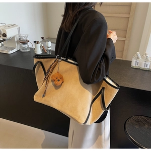 Detail of khaki suede tote bag with black leather trim and plush dog charm in cafe setting