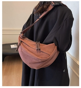 Detail of a dark brown suede crescent crossbody bag with a wide nylon strap on model
