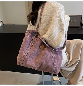 Detail of a large purple denim tote bag with brown leather patch and wide shoulder strap