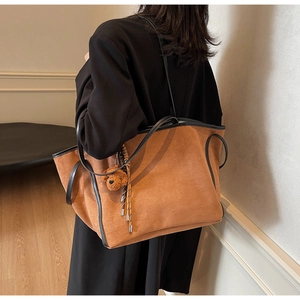 Brown suede tote bag detail with plush bear accessory and elegant black piping accents