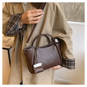 Close-up of brown pebbled leather handbag with white stitching and metal chain charm