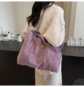 Detail of purple washed denim tote bag with brown leather logo tag in a cafe setting
