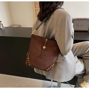 Dettaglio borsa a secchiello marrone opaco con borchie dorate su una modella
