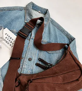 Detail view of coffee canvas crossbody bag with adjustable wide strap and buckle on denim jacket