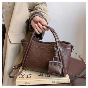 Detail of coffee PU leather bag with white stitching and mini charm on a book