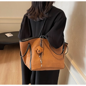 Brown suede tote bag with plush bear charm shown on model in a minimalist setting