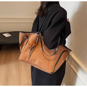 Detail of a large brown suede tote bag with black leather handles and cute bear charm