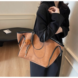 Detail of tan suede tote bag with black leather straps and a cute teddy bear charm