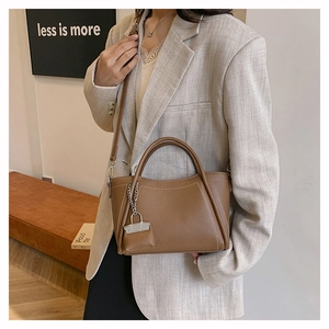 Detail of a brown lychee pattern PU leather handbag with silver lock charm and strap