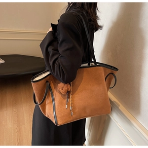 Detail of tan suede tote bag with black handles and bear charm worn by a model