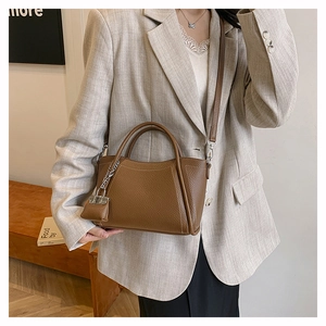 Detail view of brown pebbled leather handbag with adjustable strap and charm on shoulder