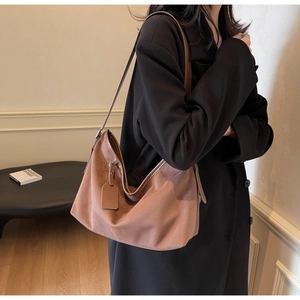 Détail de la texture d'un sac hobo en daim marron sur un mannequin en blazer noir