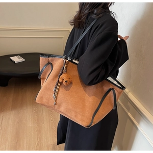 Detail view of large brown faux suede tote bag with black leather trim and bear charm