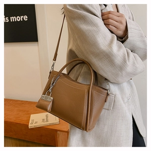 Close-up of brown litchi grain PU leather handbag with decorative mini pouch and metal chain