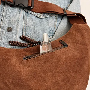 Brown suede crossbody bag detail showing front zipper pocket storage with a perfume bottle