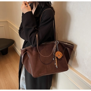 Detail of a brown PU leather tote bag with a plush bear charm on a model's shoulder
