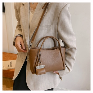 Detail of dark brown leather tote bag with mini charm and adjustable strap worn by model