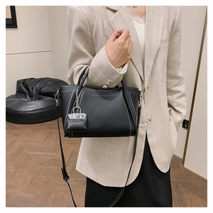 Detail of black pebbled leather tote bag with white contrast stitching on beige blazer