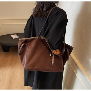 Detail of a brown suede tote bag with leather handles and a plush bear charm on side