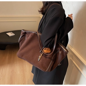 Detail of a large brown PU leather tote bag with a plush bear charm and metallic tassel