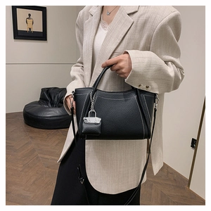 Detail of black pebbled PU leather handbag with white contrast stitching and mini lock charm
