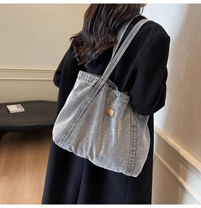 Close-up of light blue washed denim tote bag with wide straps and vintage brown label
