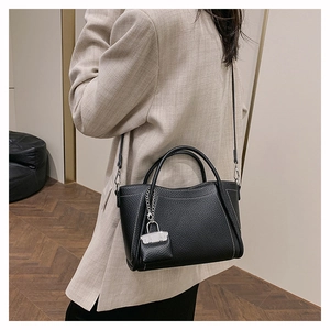Detail of a black lychee texture leather tote bag worn with a casual beige suit outfit