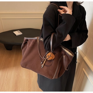 Detail of a brown suede tote bag featuring slim leather straps and a plush bear charm
