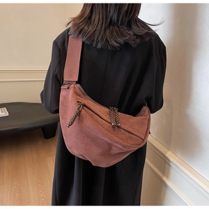 Detail of dark brown suede crossbody bag with wide strap and woven zipper puller