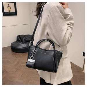 Detail of black lychee grain PU leather tote bag with white contrast stitching and mini charm