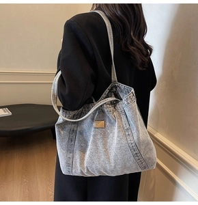 Detail of light blue denim tote bag with brown leather patch and dual shoulder straps