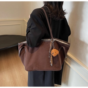 Detail of a large brown suede tote bag with leather straps and a cute dog charm