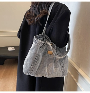 Detail of grey washed denim tote bag with leather logo patch shown on female model