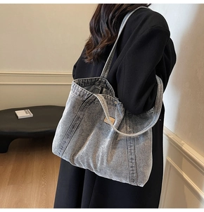 Detail of grey washed denim tote bag with brown leather tag and long shoulder straps