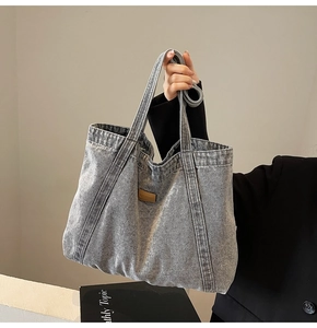 Detail of grey washed denim tote bag with brown leather patch and premium fabric texture