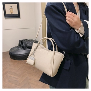 Detail of a cream faux leather tote bag with lychee texture and silver hardware shown on model