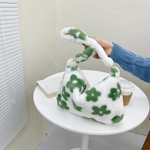 Close-up of white plush handbag with green floral pattern and gold metal ring handle