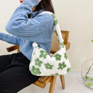 Close-up of white plush shoulder bag with green floral pattern on blue knit sweater