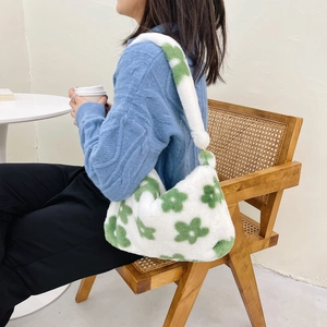 Detail of plush white shoulder bag with green flower patterns worn by a model in sweater