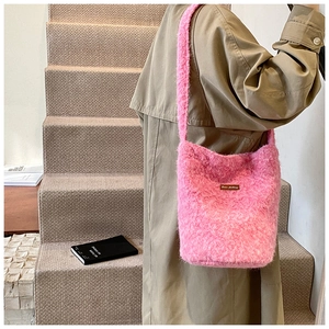 Détail du sac seau rose en fausse fourrure avec patch logo en cuir et longue bandoulière