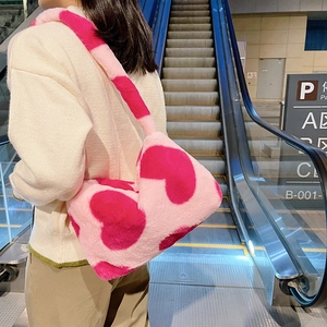 Détail d'un sac à épaule en peluche rose avec motifs de cœurs porté par un mannequin