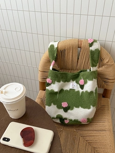 Detail of plush knit shoulder bag with green wavy patterns and 3D pink flowers on a chair