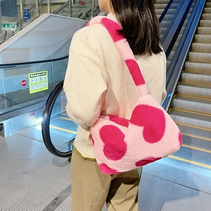 Détail d'un sac à épaule en peluche rose avec motif de cœur porté par une personne