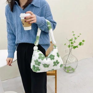 Detail showing the white and green floral plush shoulder bag worn by a model in a cozy setting