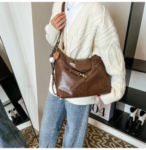 Brown leather hobo bag with gold metal buckle and baseball charm shown on a model