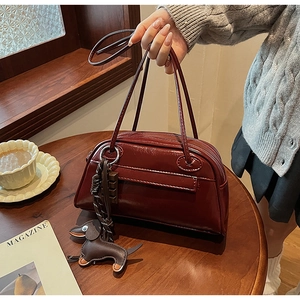 Detail of burgundy glossy PU leather handbag featuring a cute dog charm in a cafe setting
