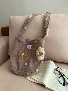 Detailed plush brown shoulder bag with decorative flowers and woven label in a cozy setting