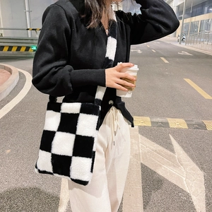 Detail of plush black and white checkered tote bag held by a model in a street style setting